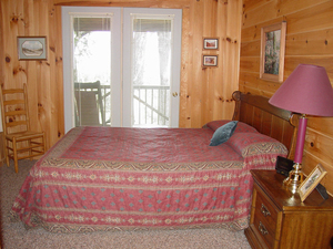 Queen bedroom with knotty pine walls and a door to the deck